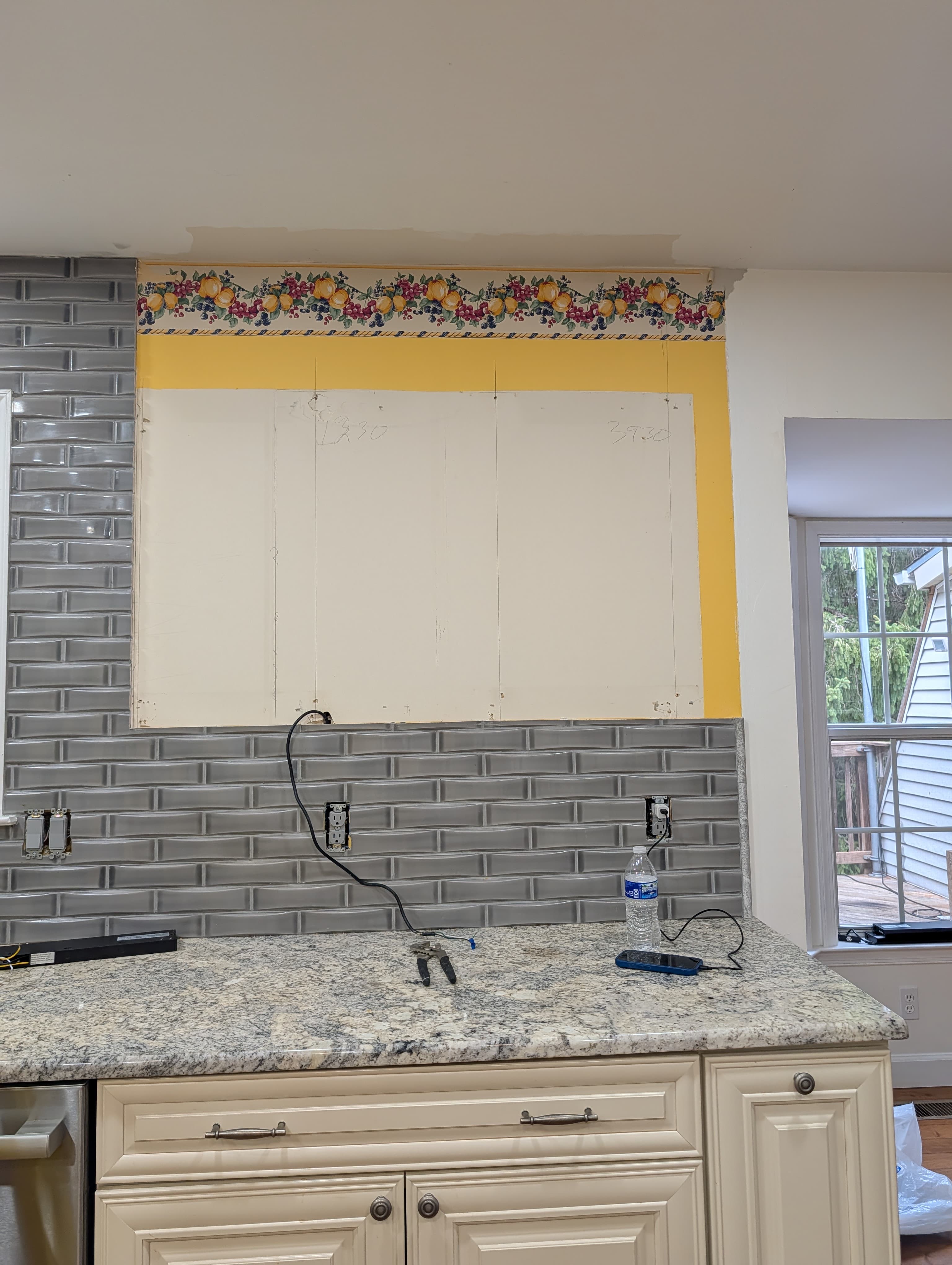 Original Herndon kitchen wall during demo, old wallpaper border above gray subway tile and a patched drywall section